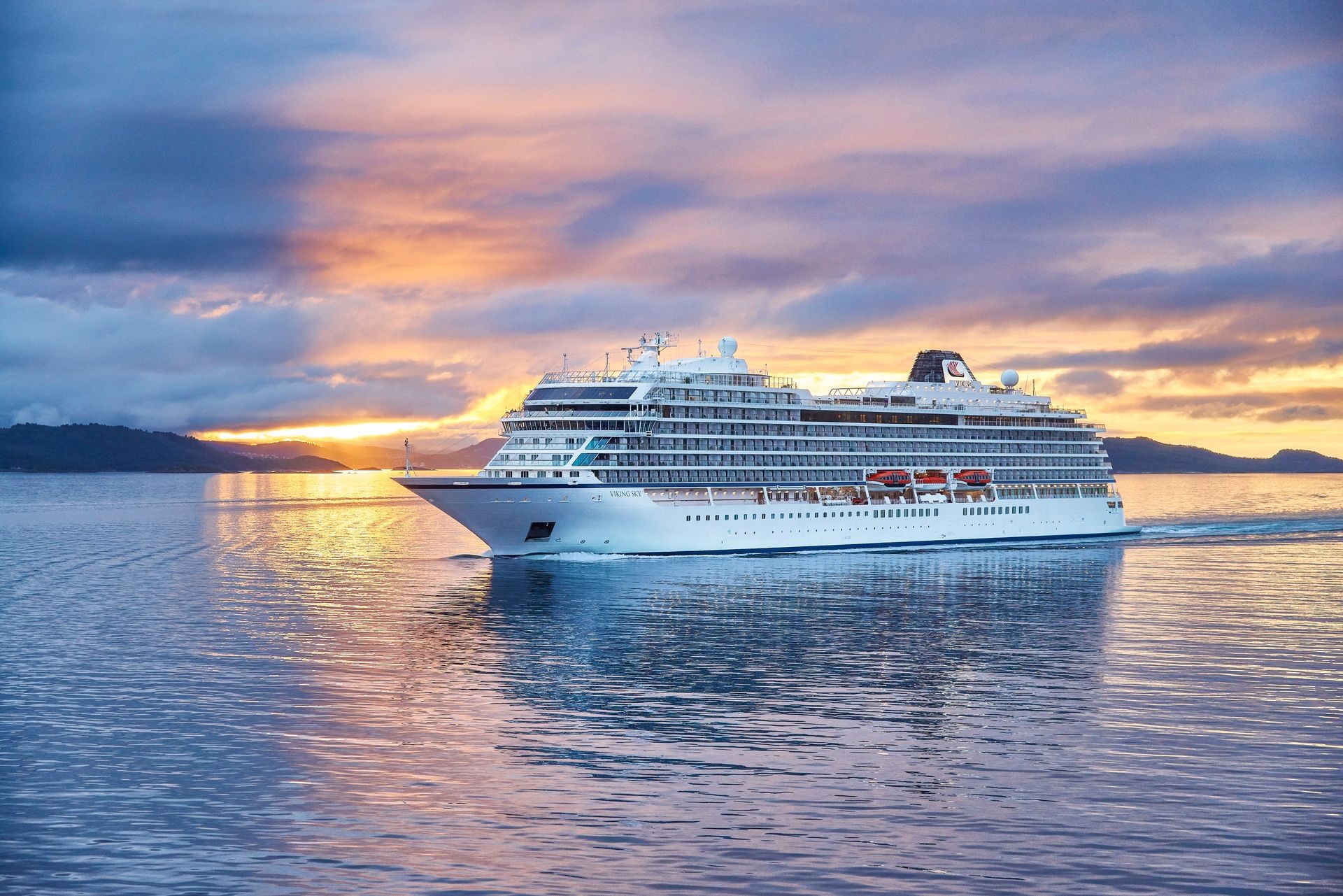 Viking Cruise ship sailing through calm waters at sunset, surrounded by scenic views of the Lofoten Islands, Norway, under a dramatic sky with hues of orange and purple. Perfect for luxury travel enthusiasts seeking unforgettable ocean voyages