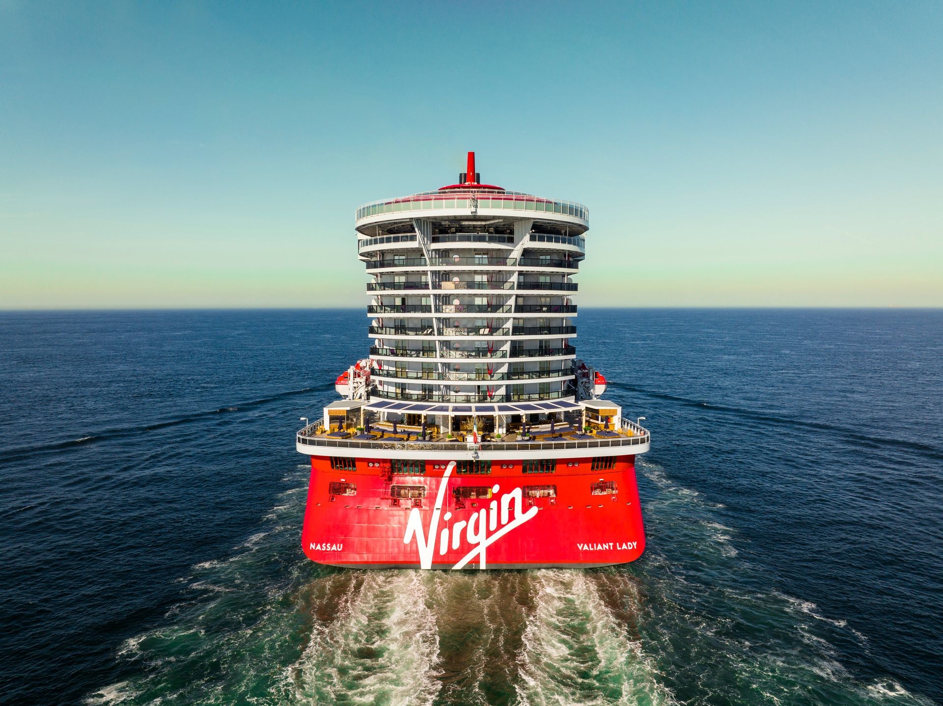 Virgin Voyages' Valiant Lady cruise ship sailing across the open ocean, showcasing its bold red exterior and modern design. A luxurious, adults-only cruise experience perfect for travelers seeking style, relaxation, and adventure.