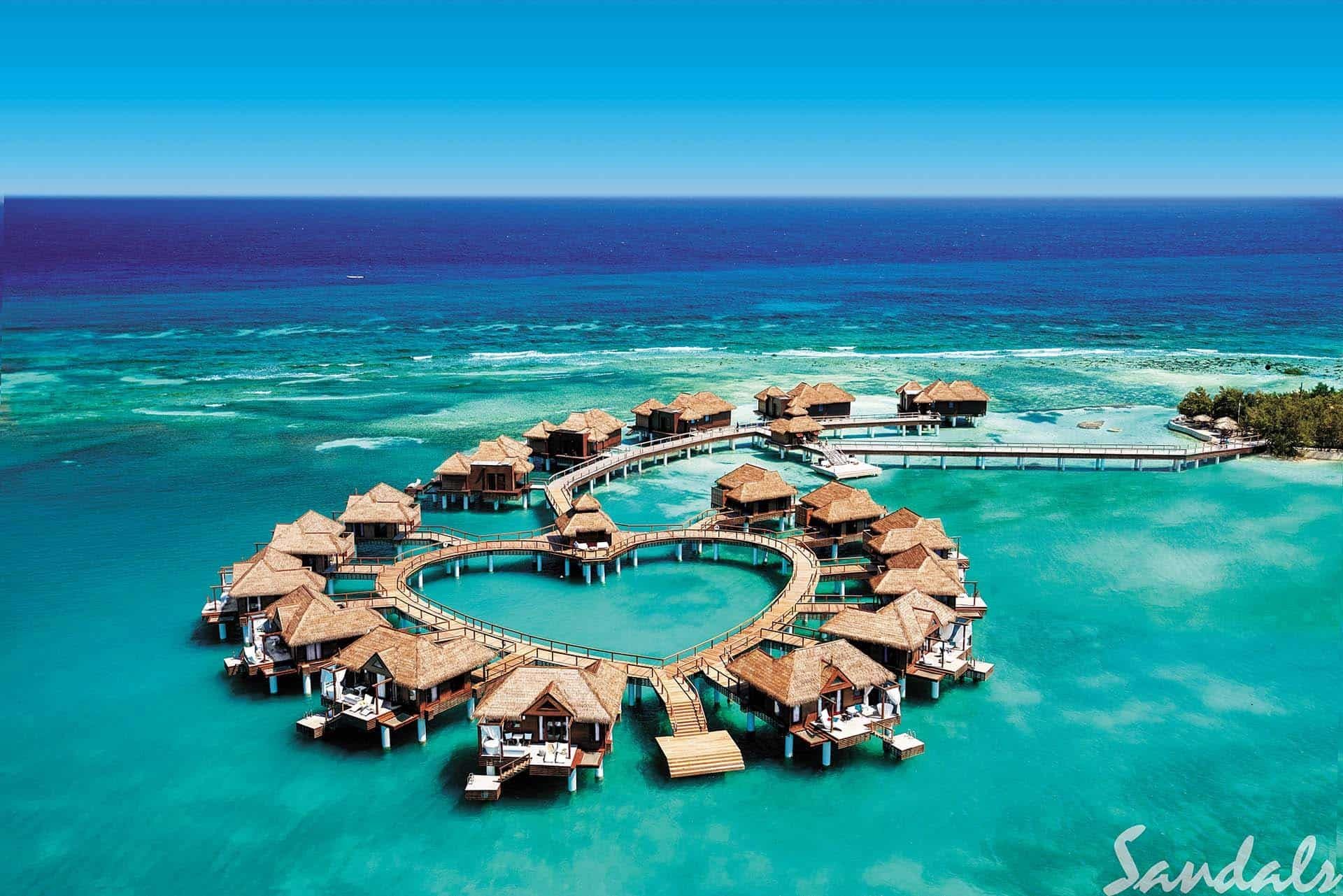 Overwater bungalows forming a heart shape at a luxurious Sandals Resort in the Caribbean, surrounded by turquoise ocean waters under a clear blue sky. Perfect for a romantic, adults-only all-inclusive getaway